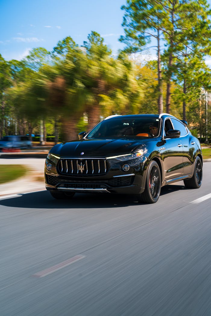 Sleek black SUV driving down a road lined with trees on a sunny day, showcasing luxury and style.